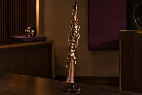Saxophone soprano droit en bronze rouge à motif sculpté, présenté sur un support en bois sombre.