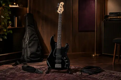 Basse électrique noire quatre cordes sur support, avec housse, sangle et câble dans un studio