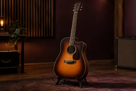 Guitare acoustique dreadnought cutaway au fini sunburst mat, posée sur un support dans un studio chaleureux.
