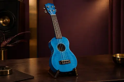 Ukulélé soprano bleu Donner en érable, posé seul sur un support dans un décor de studio chaleureux.