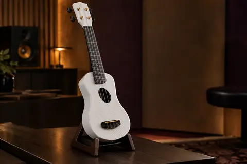 Ukulélé soprano blanc en fibre de carbone, posé seul sur un support en bois sombre dans un studio.