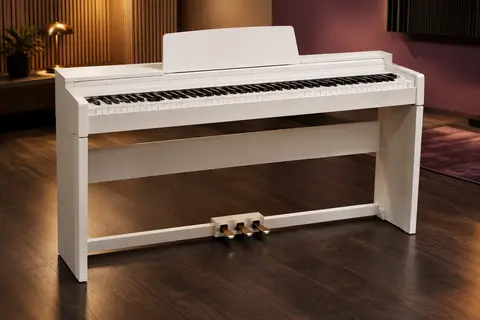 Piano numérique blanc à 88 touches lestées avec pédalier triple dans un studio épuré.
